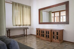 A room with a wooden cabinet, a table with a patterned tablecloth, and a large mirror on the wall. - Matthew Villa Umalas (Kerobokan)