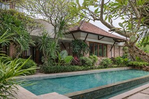 A poolside area with a brick building, surrounded by lush greenery and a tiled swimming pool. - Matthew Villa Umalas (Kerobokan)