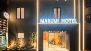 The exterior of Marumi Hotel with a modern design, illuminated signage, and a welcoming entrance.