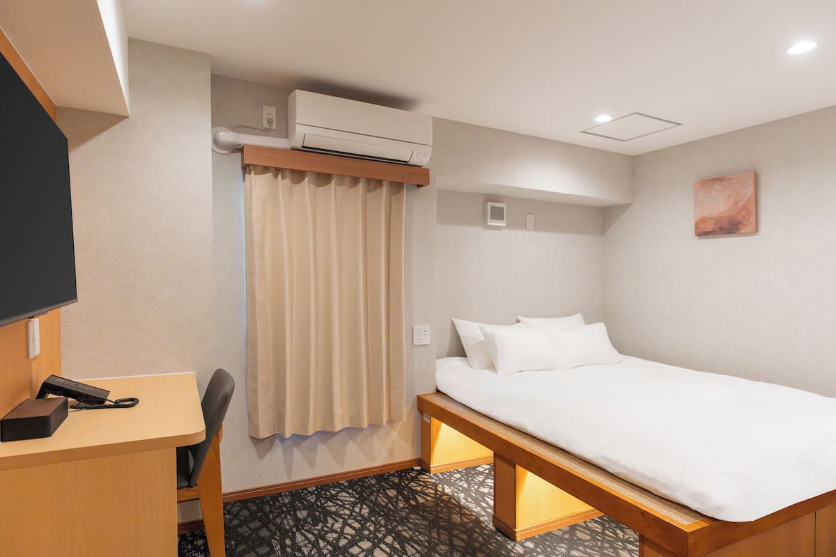 Camera d'albergo con un letto, una scrivania, una sedia, un condizionatore d'aria e un quadro appeso al muro.