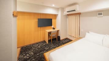 Een hotelkamer met een bed, een bureau met een stoel, een televisie, een airconditioning en een kamerbreed tapijt met dessin.