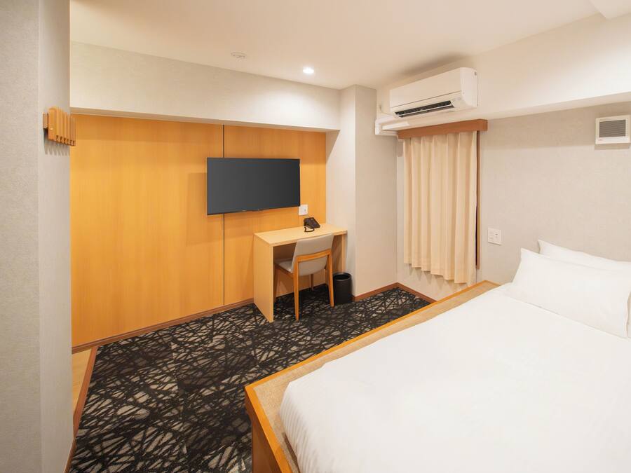 Een hotelkamer met een bed, een bureau met een stoel, een televisie, een airconditioning en een kamerbreed tapijt met dessin.