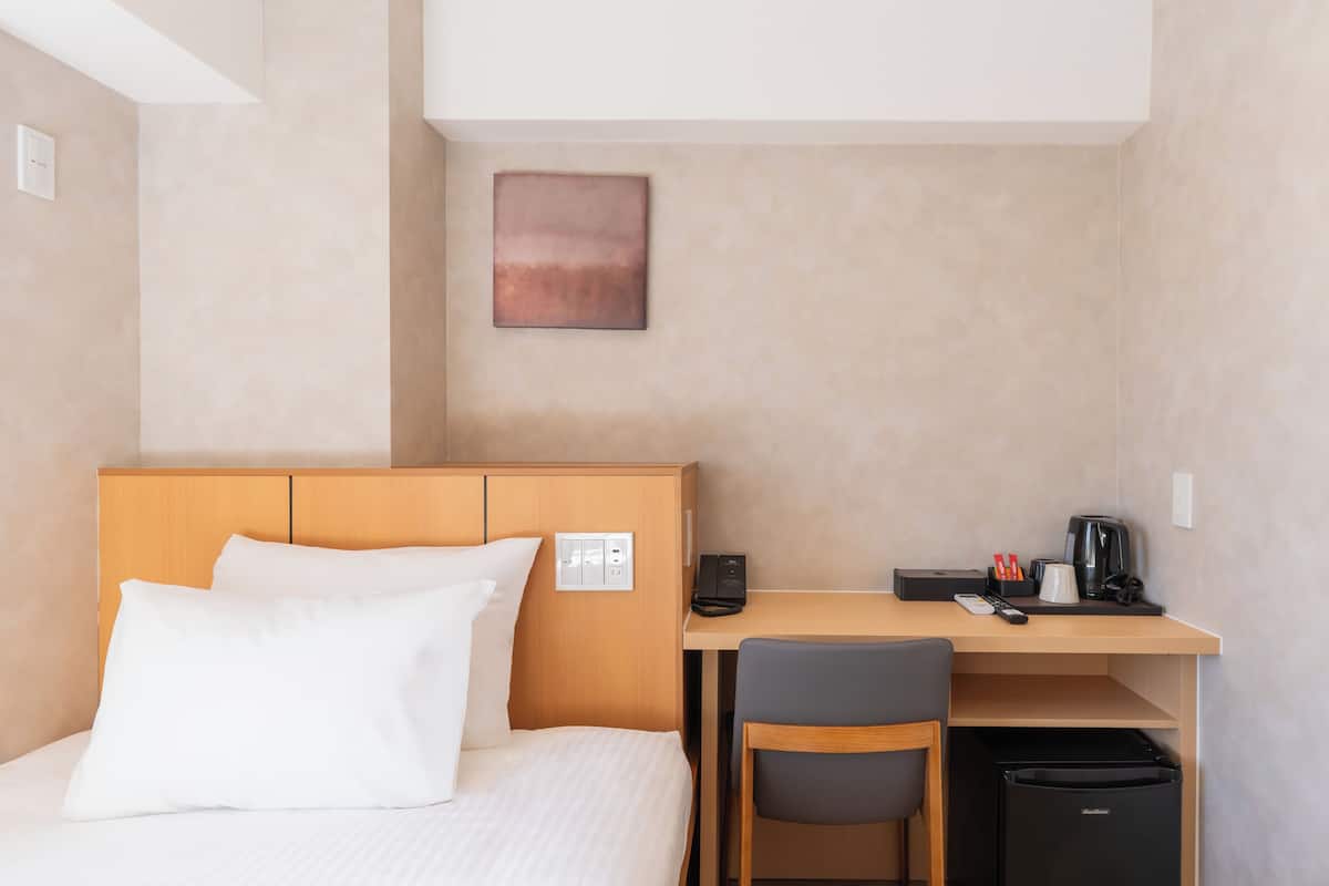 Una camera d'albergo con un letto, una scrivania, una sedia, una macchina del caffè e un frigorifero.