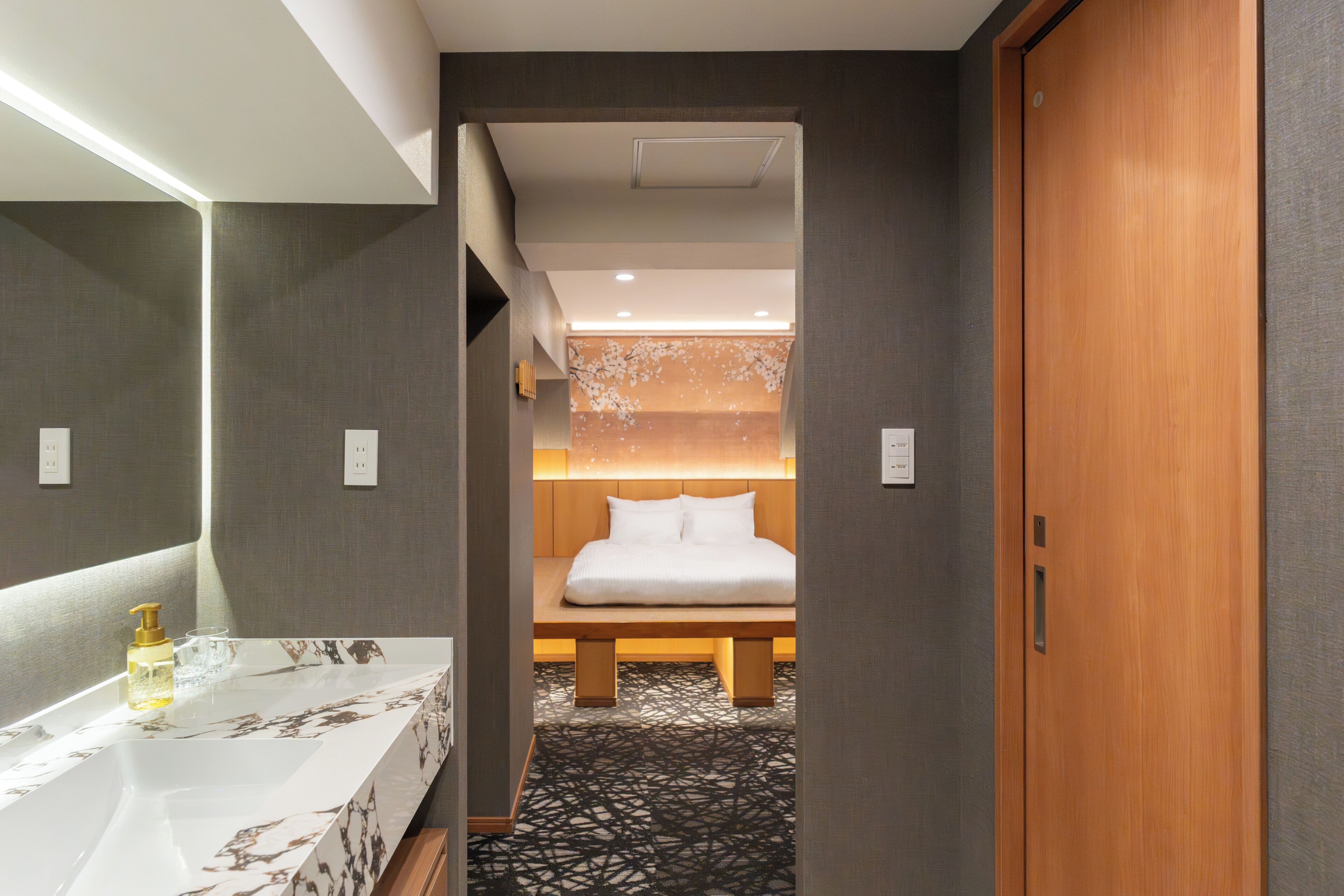 Ein Hotelzimmer mit modernem Badezimmer, einem Bett mit Holz-Kopfteil und einem Musterparkett.