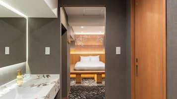Ein Hotelzimmer mit modernem Badezimmer, einem Bett mit Holz-Kopfteil und einem Musterparkett.