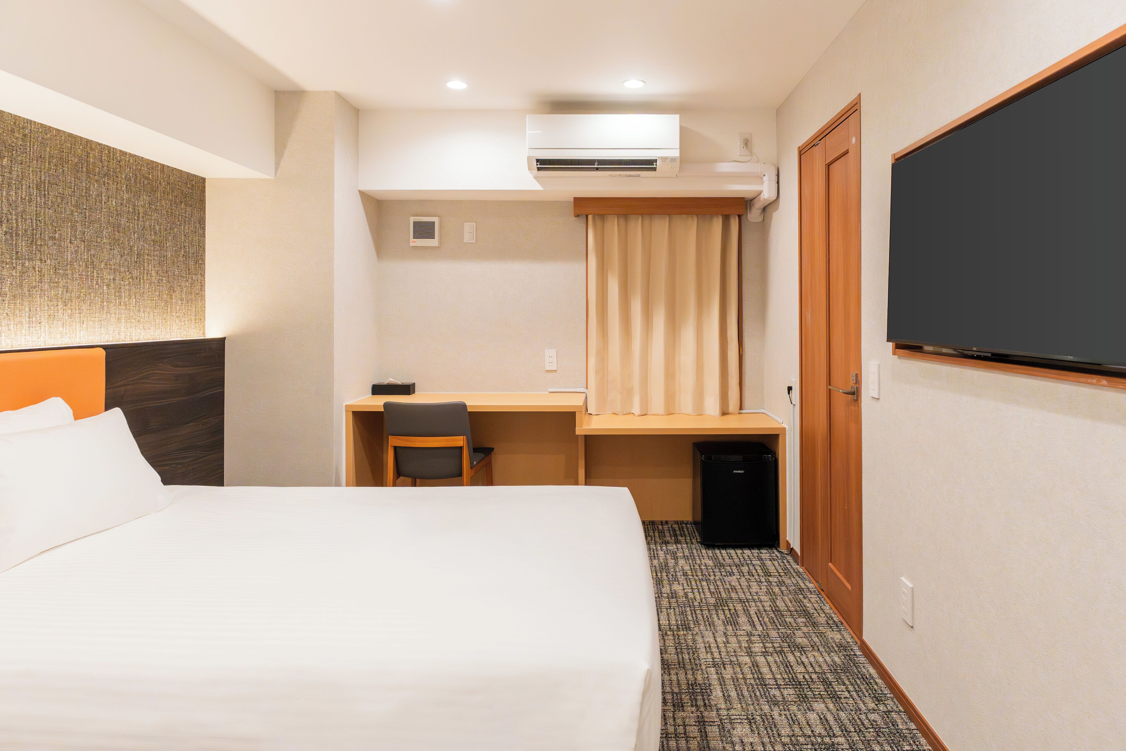 A hotel room with a bed, desk, chair, air conditioning unit, and a large blackboard.
