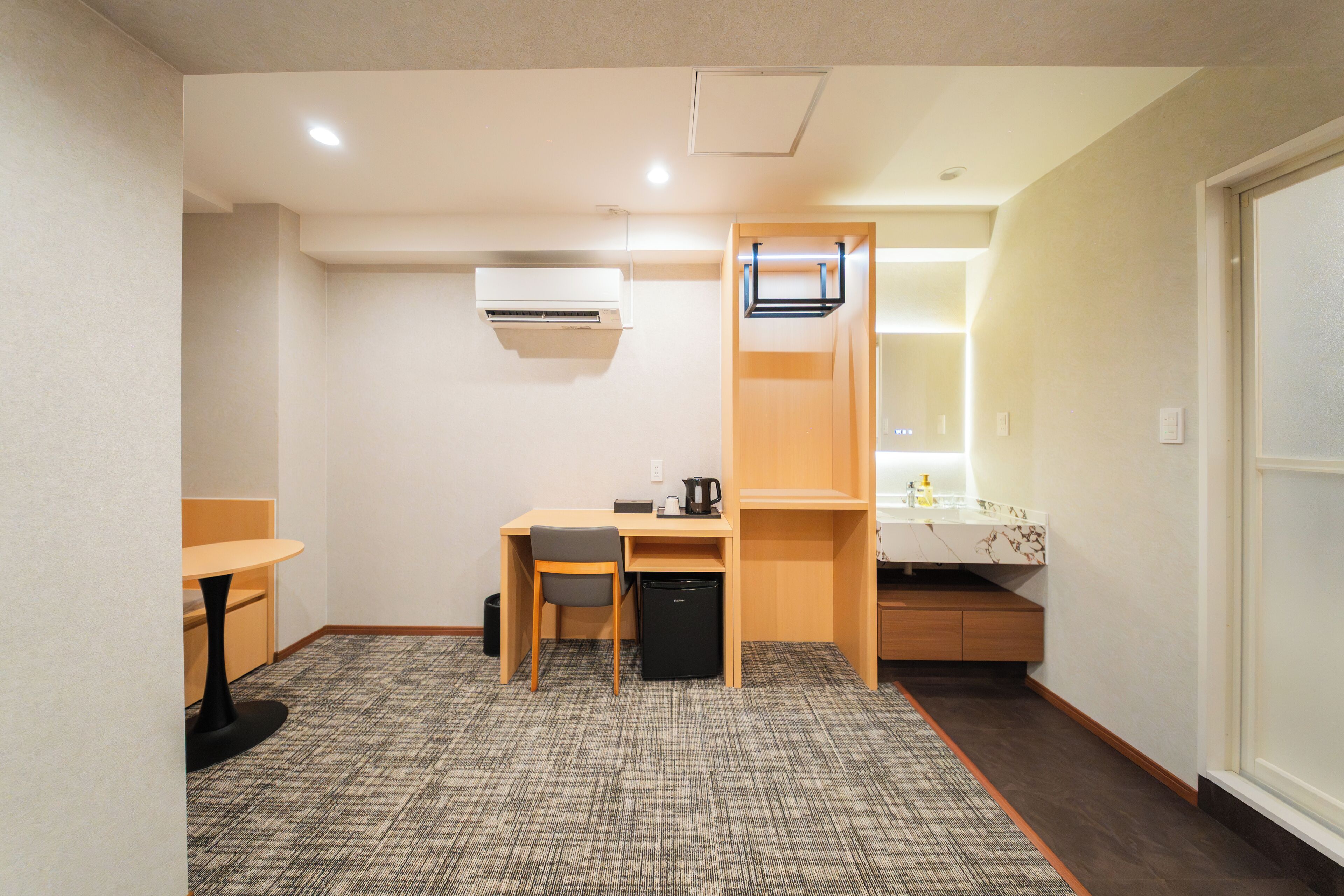 A compact hotel room with a small desk, chair, and kitchenette.