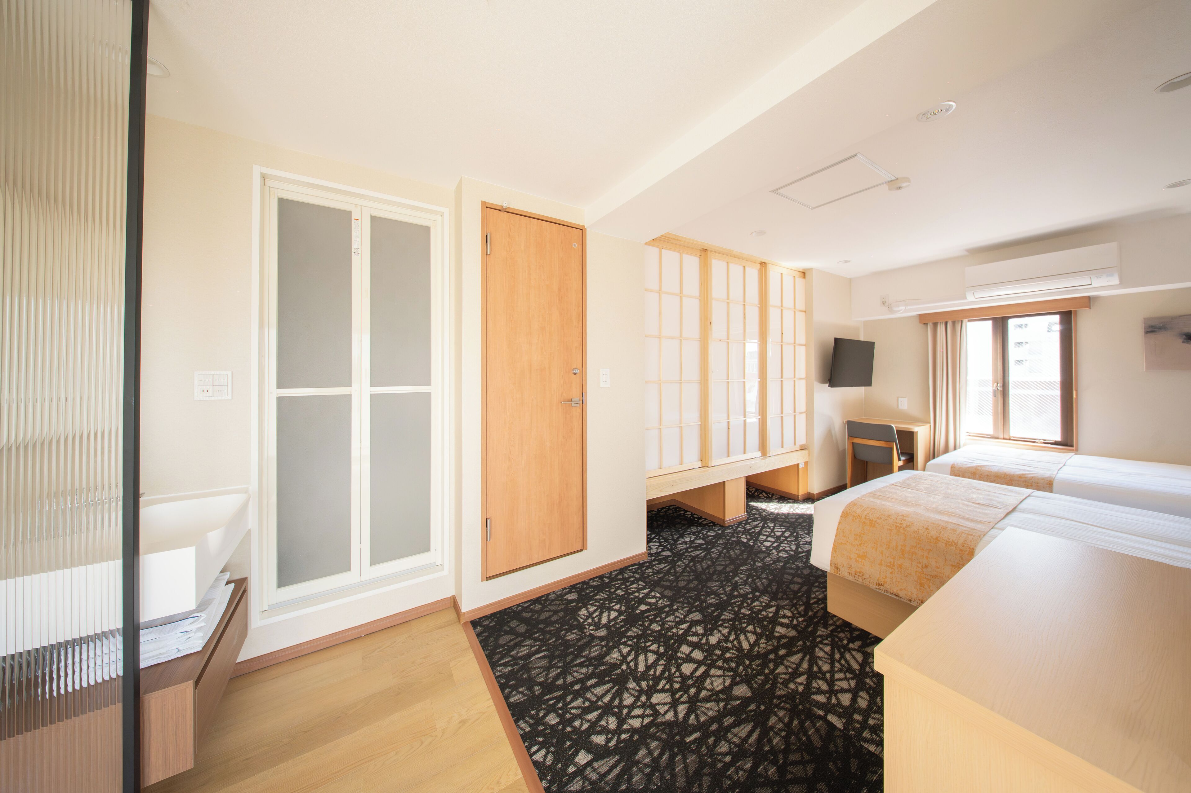 A hotel room with a wardrobe, a desk, a bed, and a television.