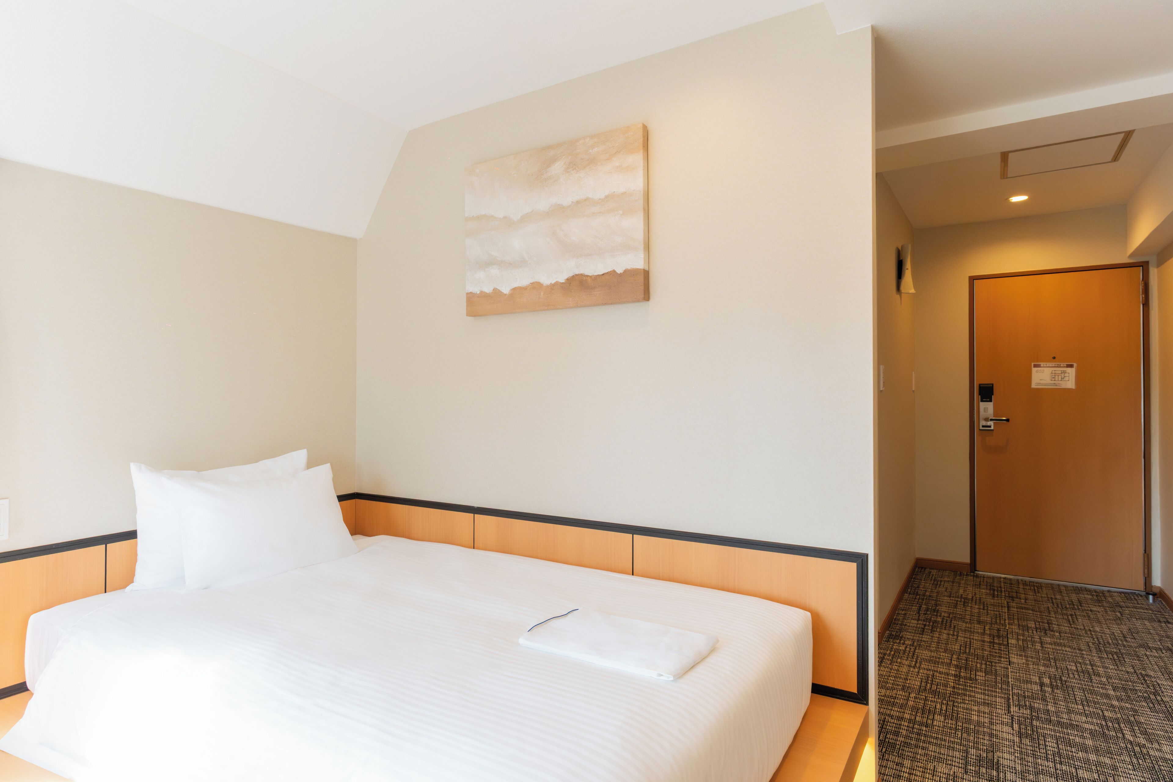Una camera d'albergo con un letto rifatto, un quadro appeso al muro e una porta che dà su un'altra stanza.