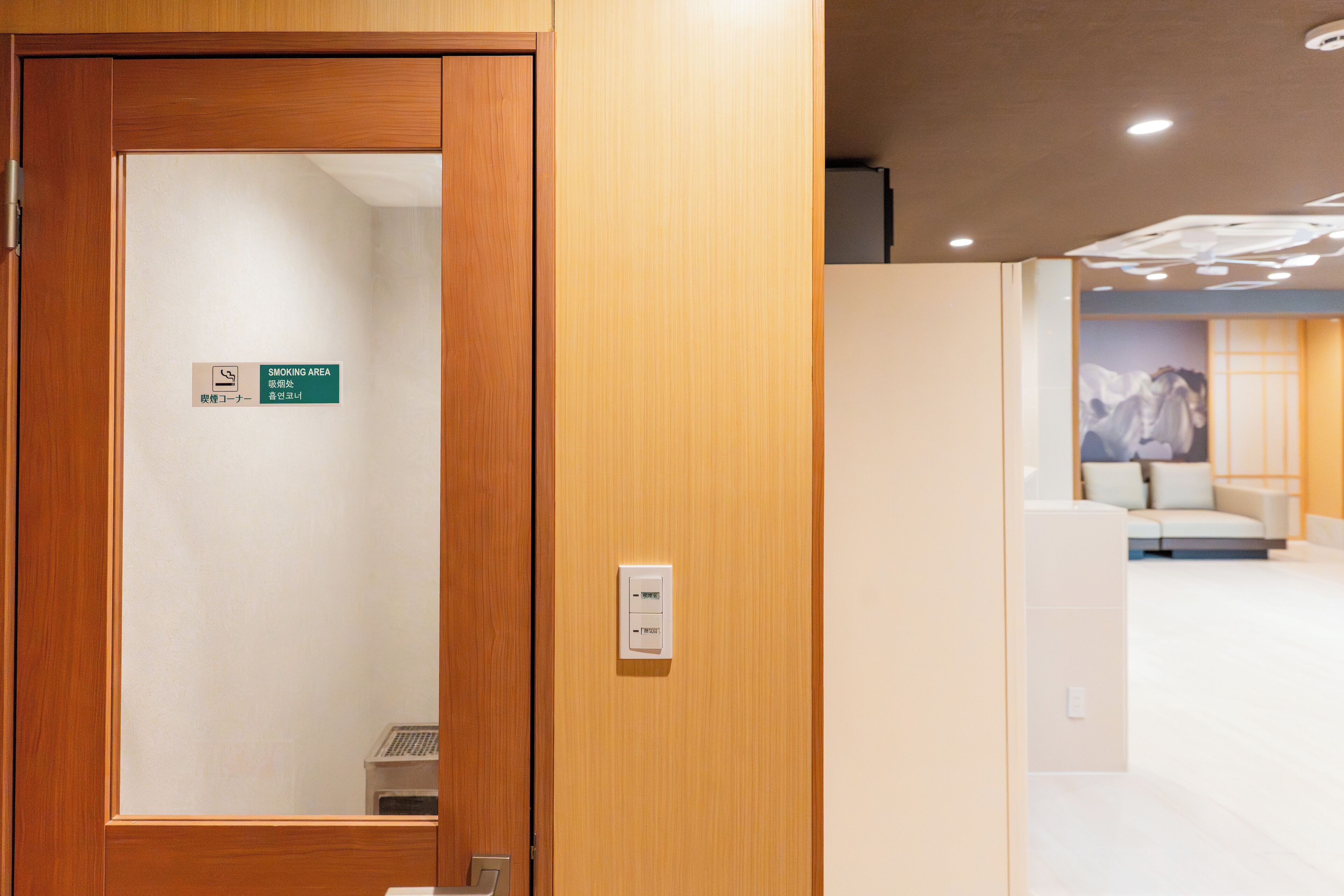 A hotel reception area with a wooden door, a sign indicating a smoking area, and a modern interior with a sofa and a lamp.