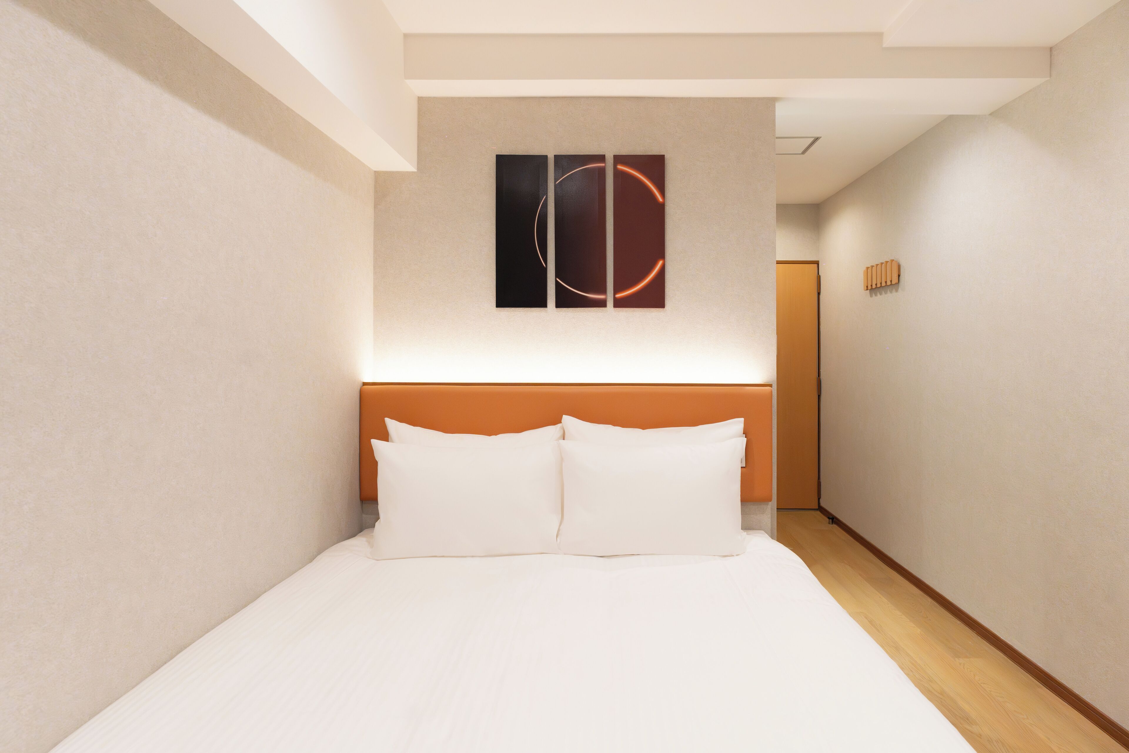 A modern hotel room with a large bed, a wooden headboard, and a minimalist wall art piece above the bed.