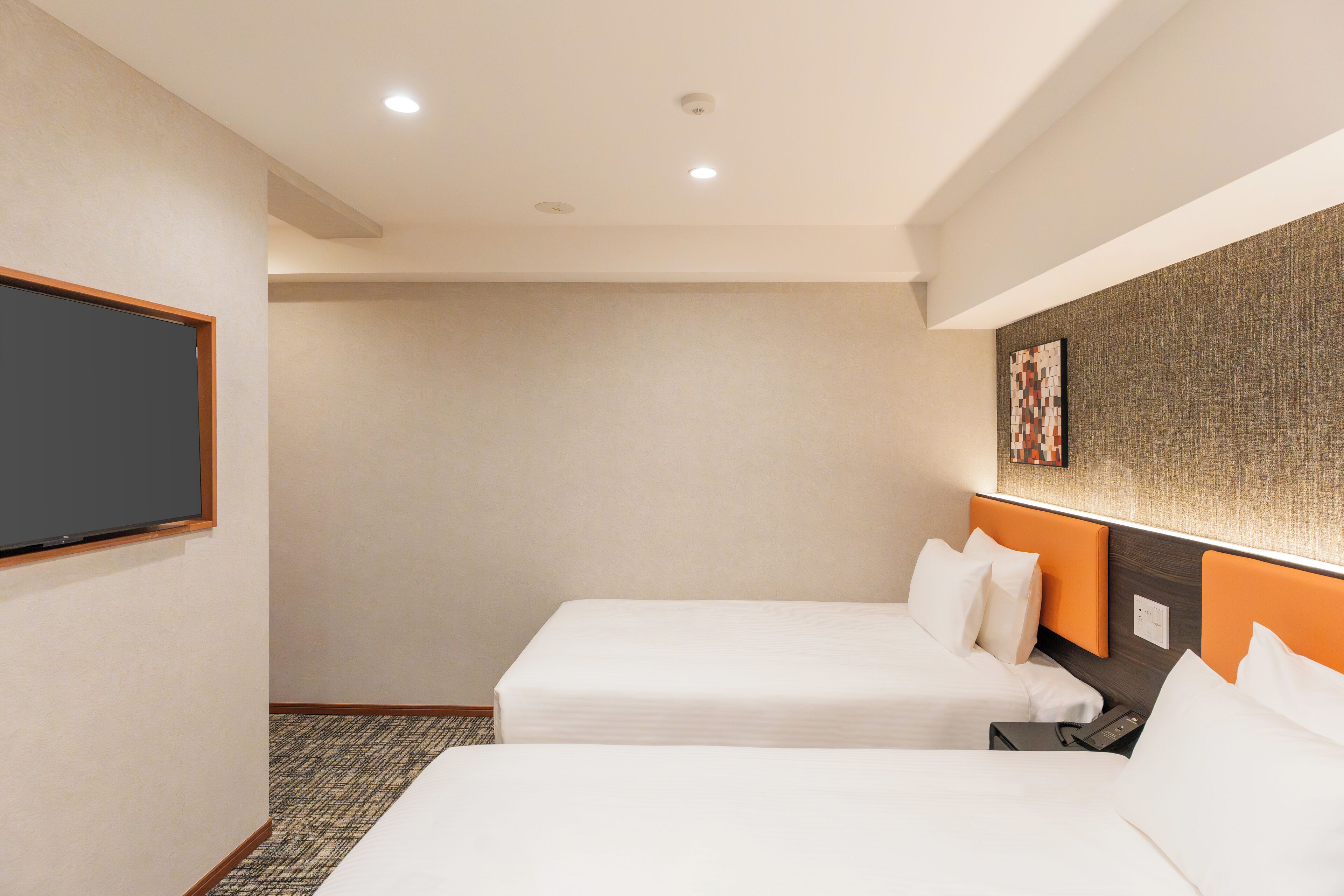 Habitación de hotel con dos camas individuales, un televisor de pantalla plana montado en la pared y una mesita entre las camas.