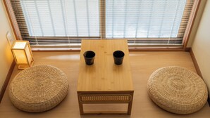 A room with a wooden table, two black cups, and two woven poufs.