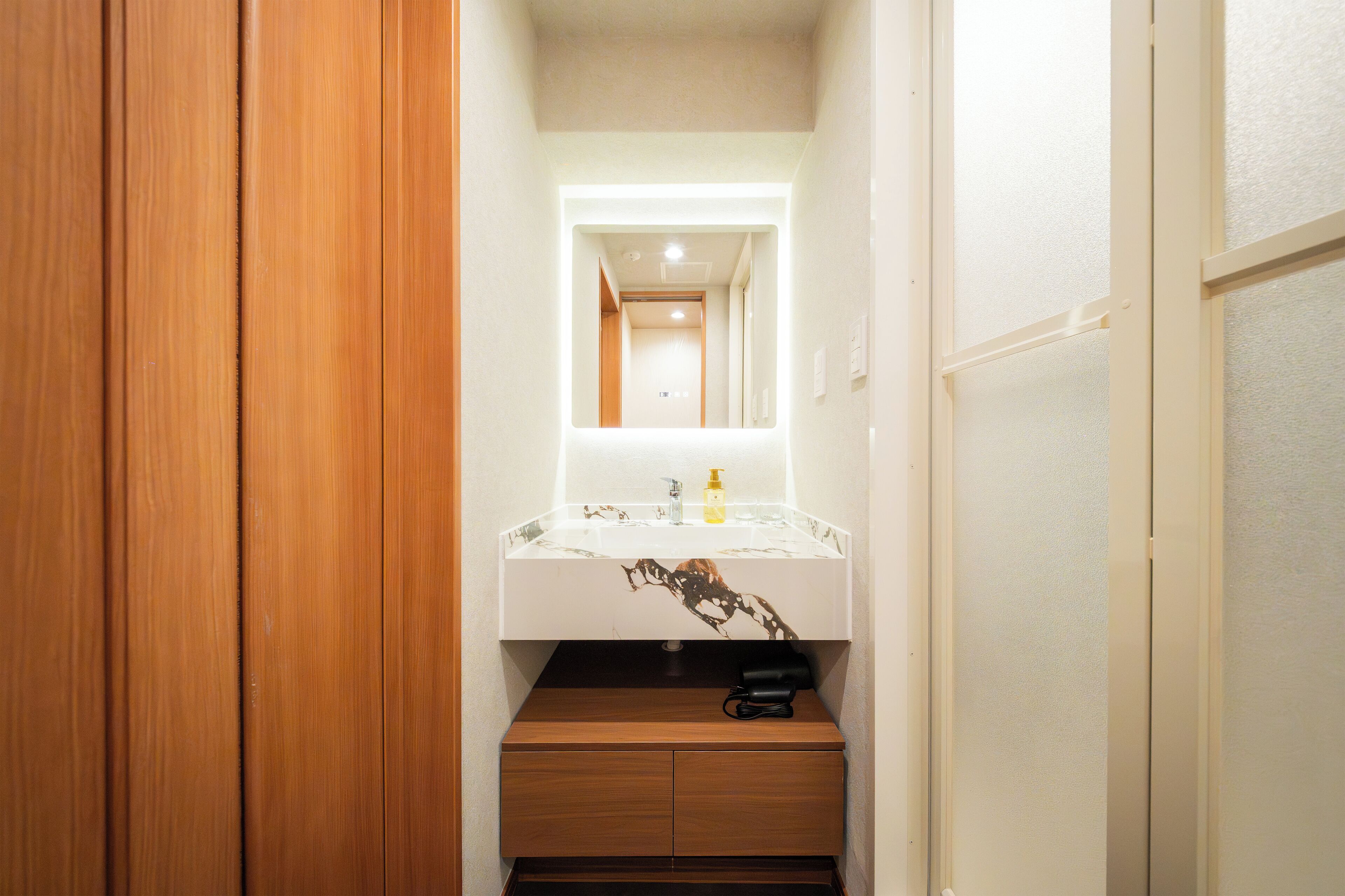 A narrow hallway leading to a bathroom with a wooden cabinet, a white sink with a marble-like backsplash, and a mirror above the sink.