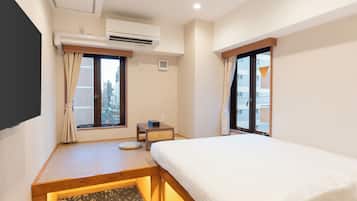 Ein Hotelzimmer mit Bett, einem kleinen Tisch, einem Sessel, einer Klimaanlage und einem fensterbepflanzten Fenster.