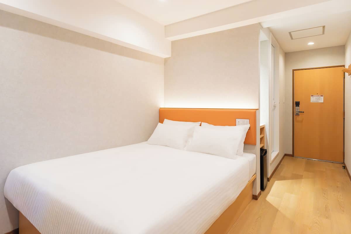 Camera d'albergo con un letto grande, pavimento in legno e una porta sulla destra.