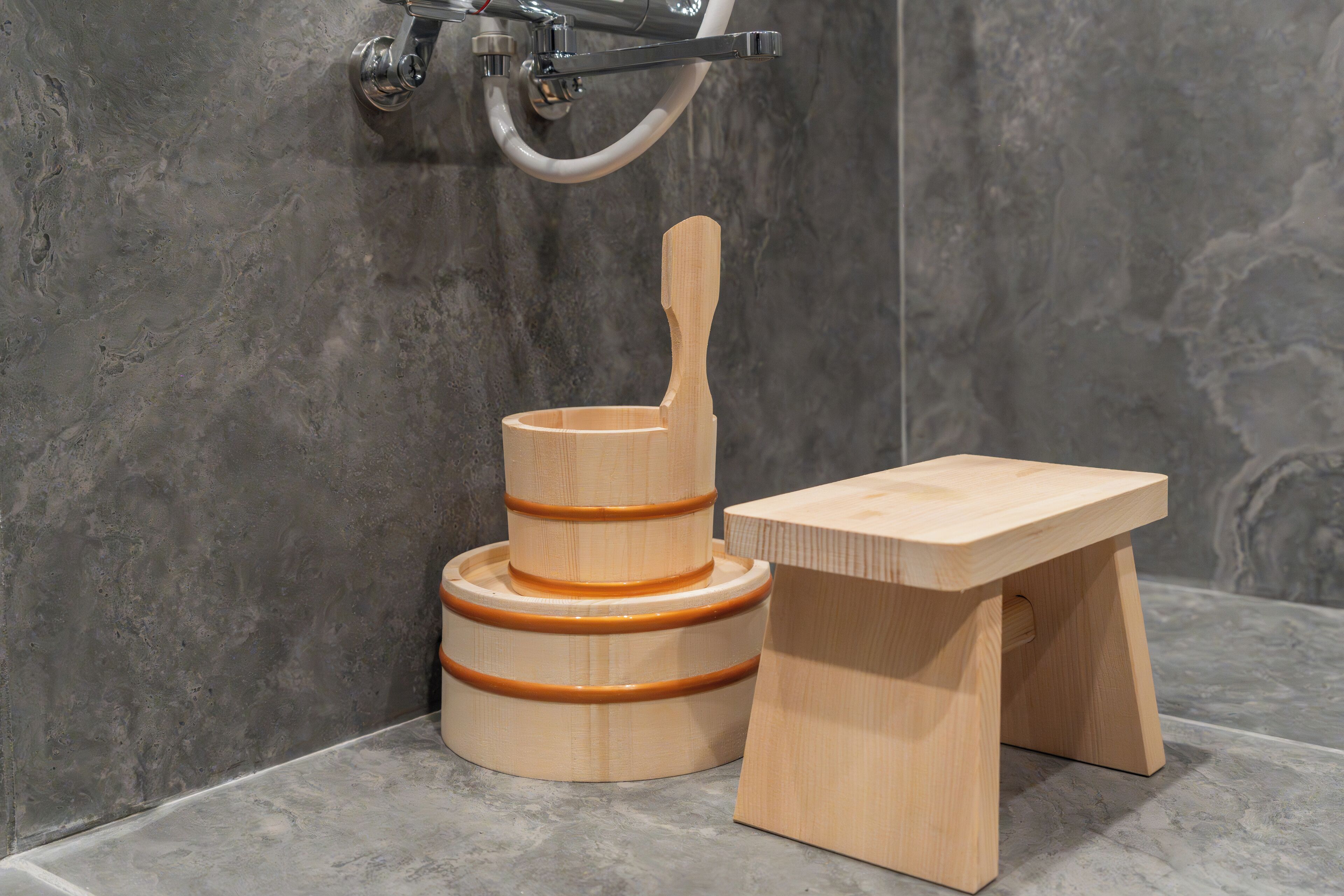 A bathroom with a wooden stool and a wooden basin with a handle.