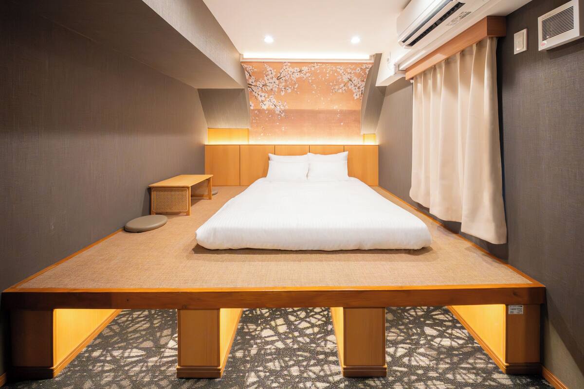 Camera d'albergo moderna con un letto grande, un comodino in legno, un tavolino e un pannello decorativo a parete.