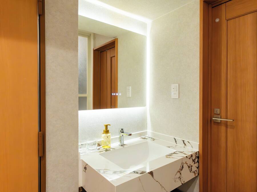 Un baño con lavamanos de mármol blanco, un espejo y puertas de madera.