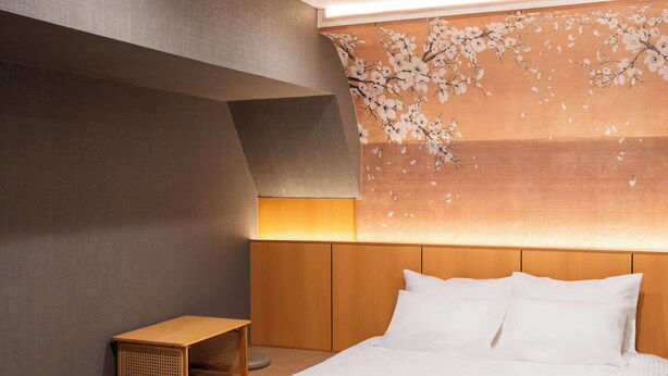 A modern hotel room with a large bed, a wooden headboard, a small wooden table, and a wall with a floral design.