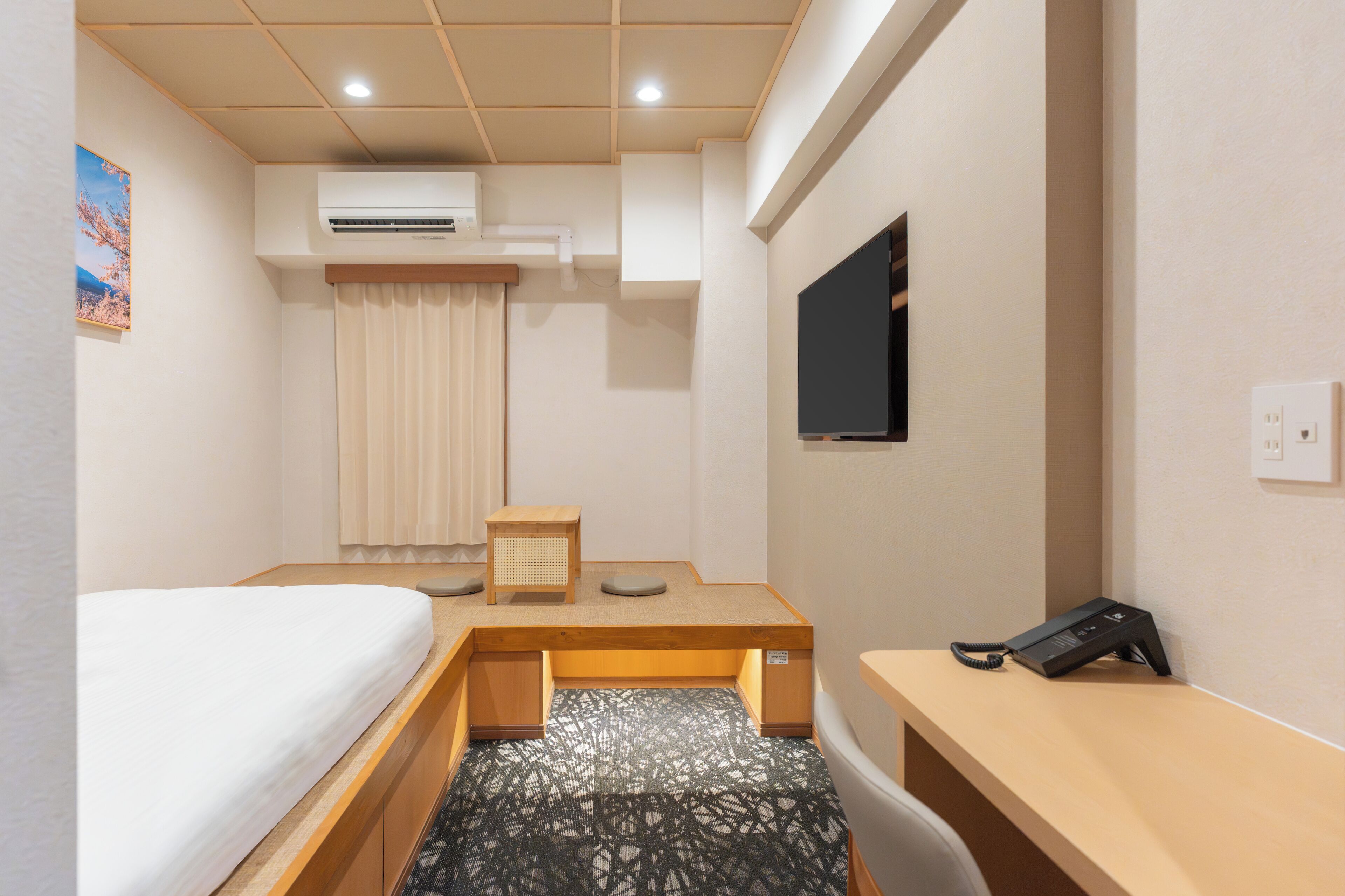 A hotel room with a bed, a desk, a chair, an air conditioning unit, a television, and a telephone.