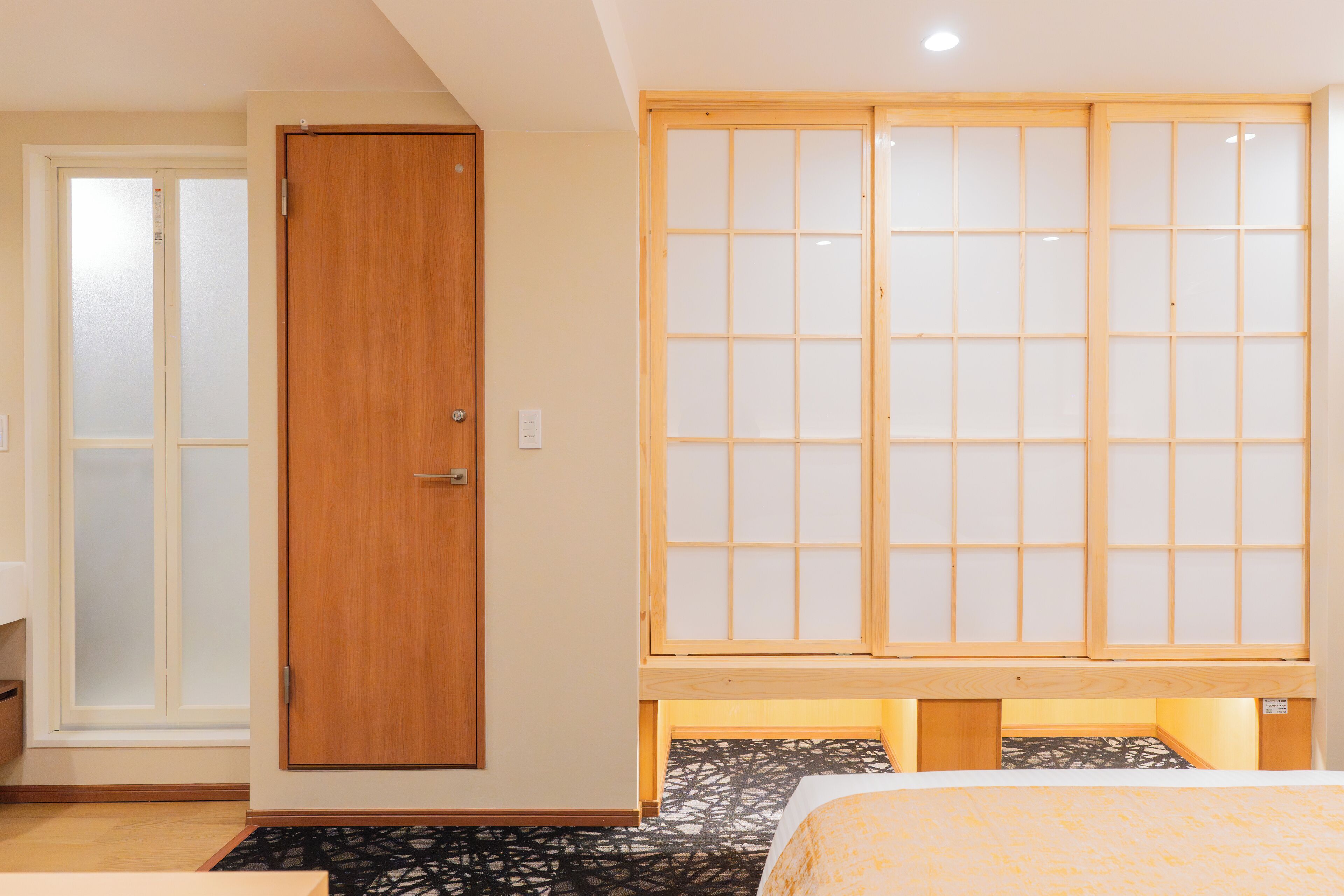 A hotel room with a wooden wardrobe, a sliding door, and a bed with a patterned bedspread.