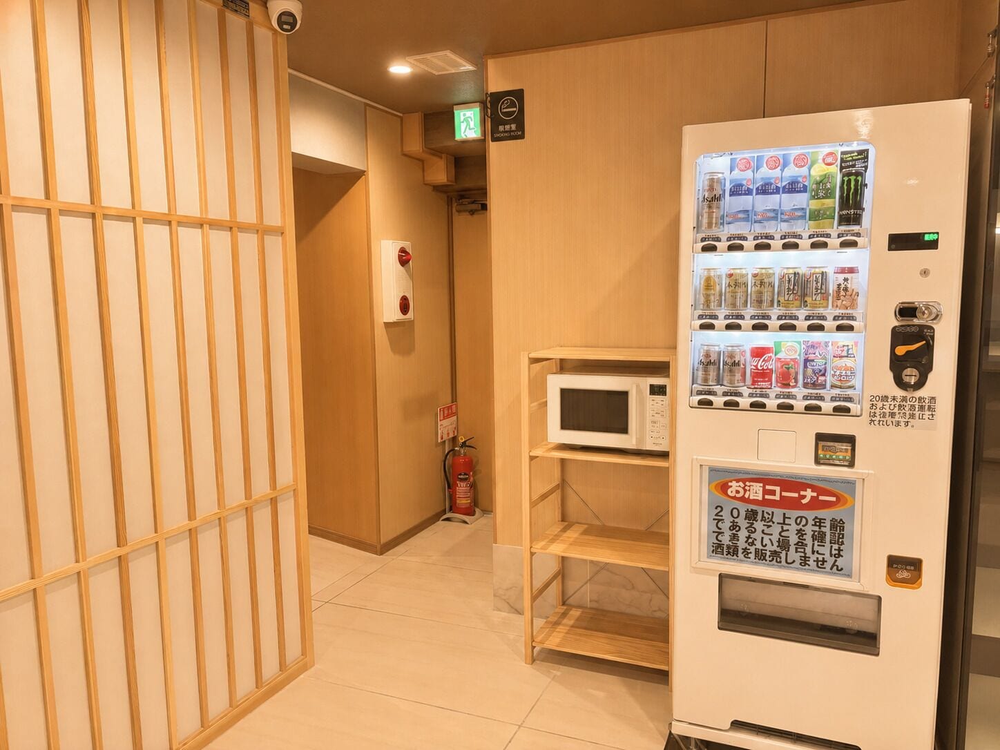Un couloir d’hôtel avec un distributeur automatique, un extincteur et un four à micro-ondes posés sur une étagère.