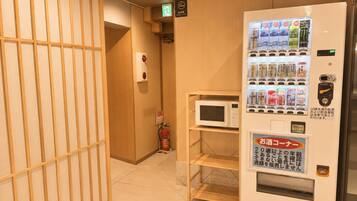 Un couloir d’hôtel avec un distributeur automatique, un extincteur et un four à micro-ondes posés sur une étagère.