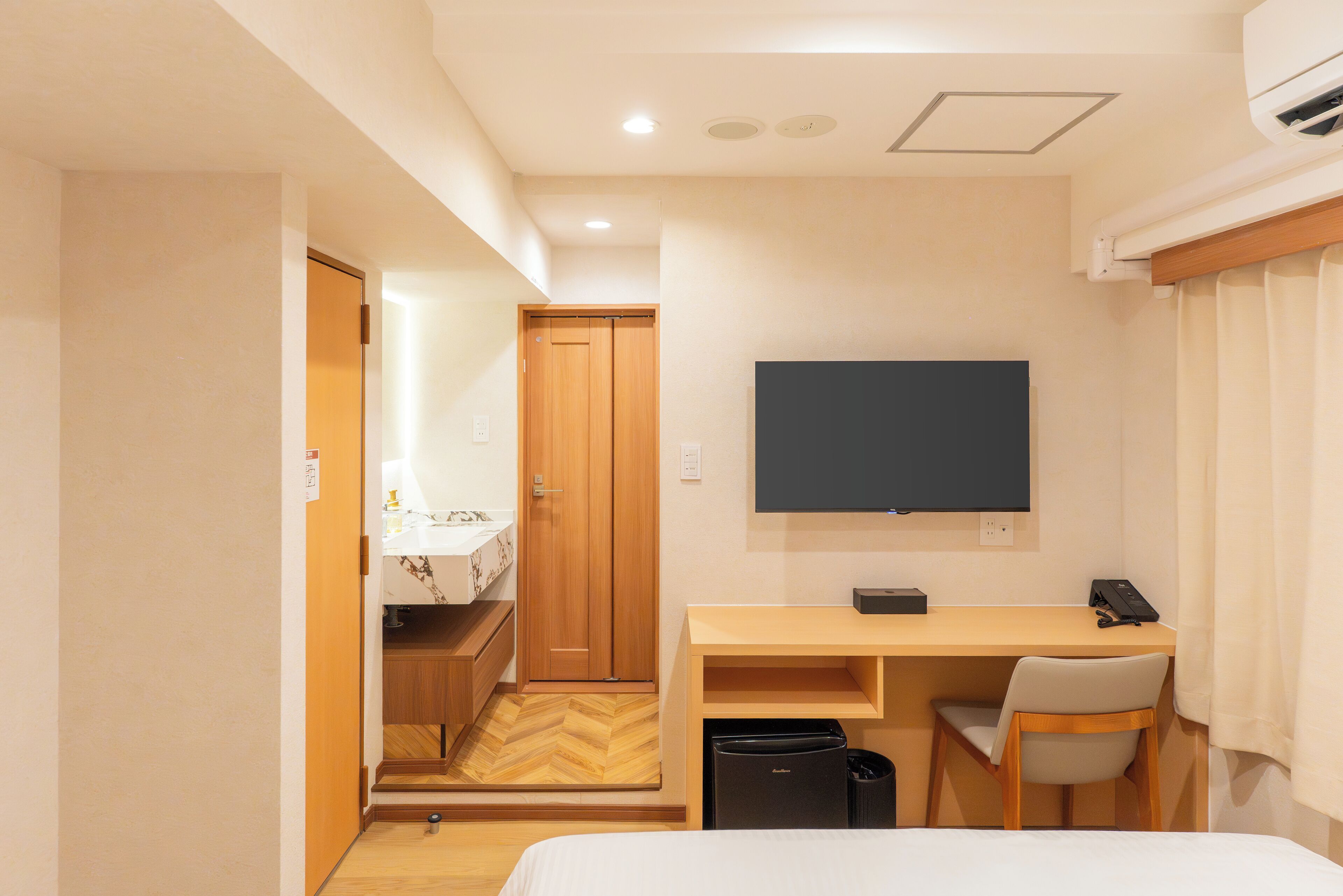 Una habitación de hotel con una cama, un escritorio con silla, un televisor y una kitchenette pequeña.