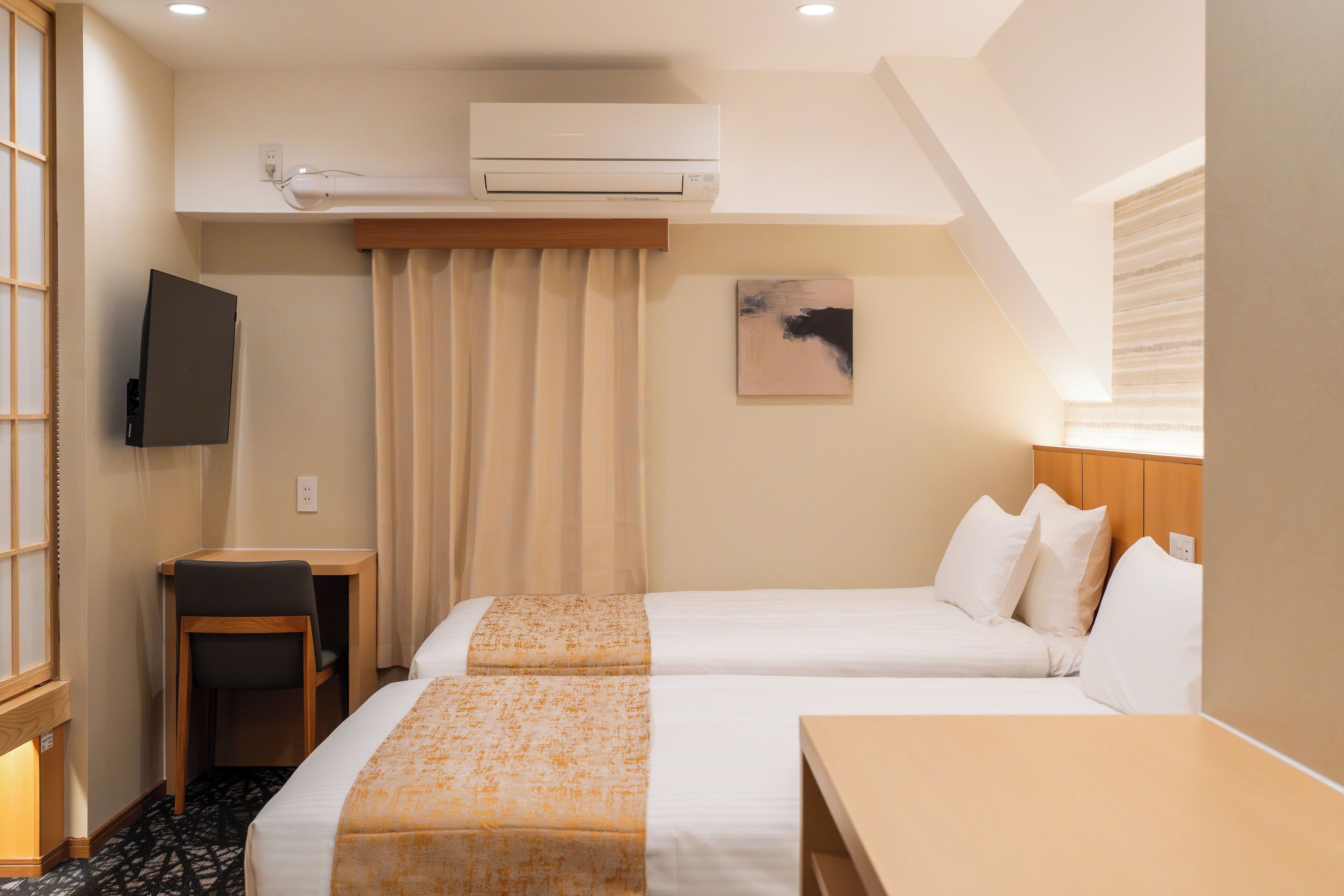 Una habitación de hotel con dos camas, un escritorio, un televisor y aire acondicionado.
