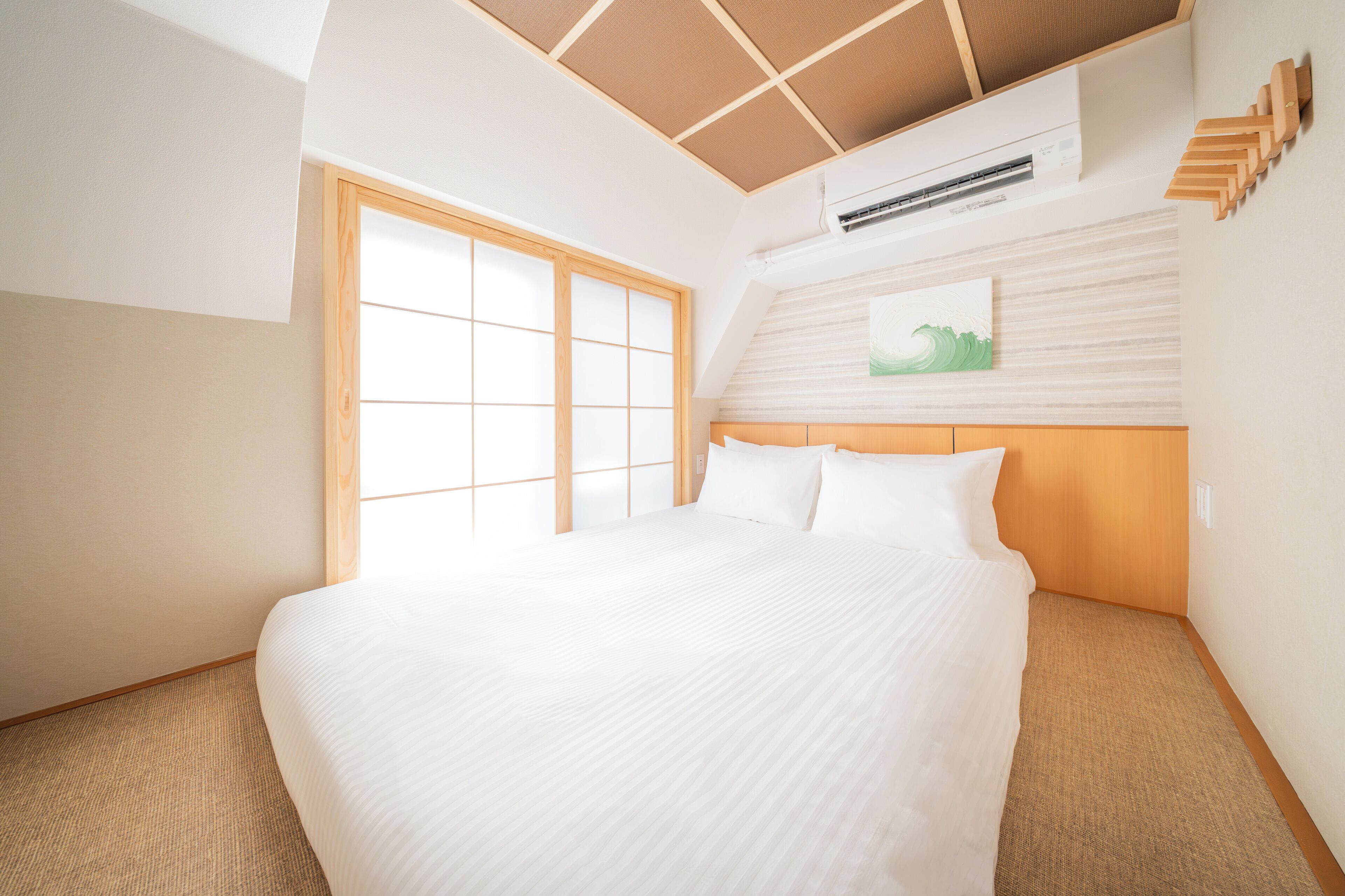 Una habitación de hotel con una cama grande, una puerta corredera de fusuma, un cabecero de madera y un aire acondicionado instalado.