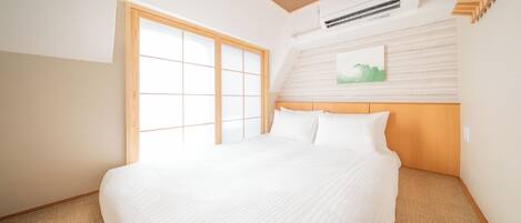 Una habitación de hotel con una cama grande, una puerta corredera de fusuma, un cabecero de madera y un aire acondicionado instalado.
