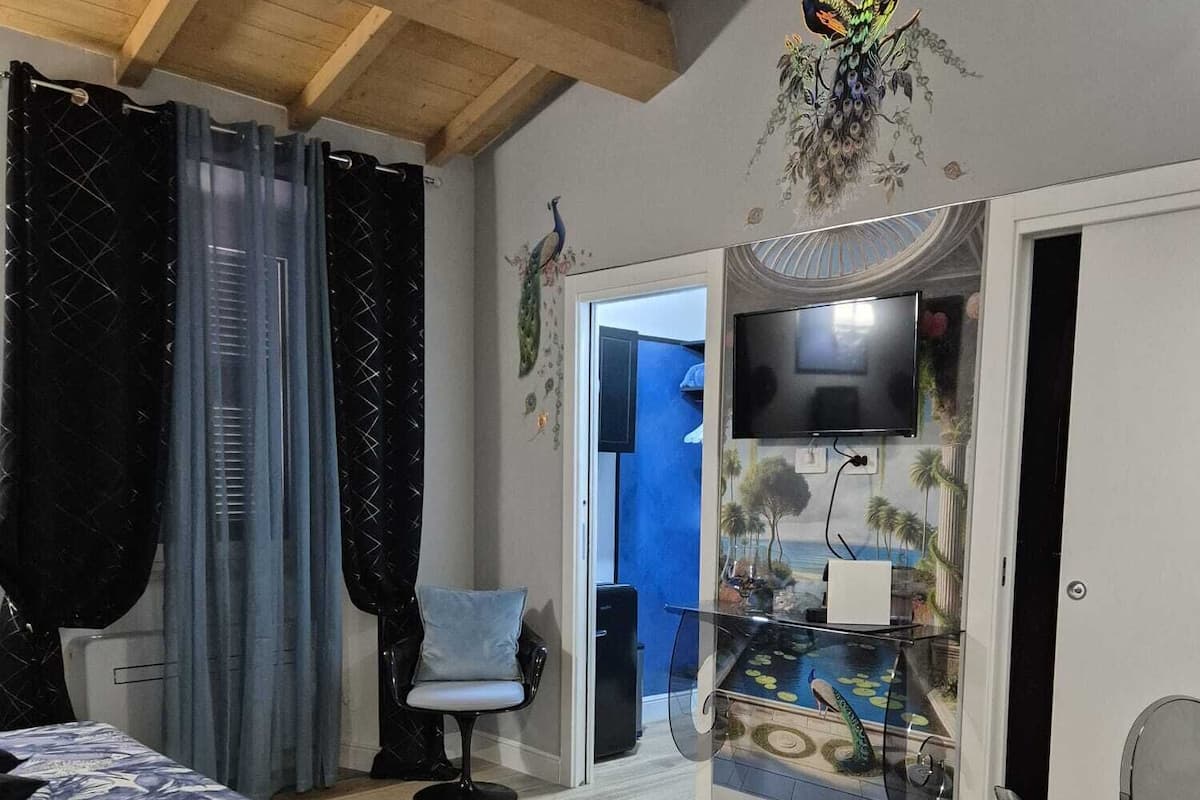 Une pièce comprenant un lit, une chaise, un téléviseur et une vitrine contenant une représentation d’un paysage tropical.