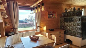 A cozy cabin interior with a wooden dining table, cushioned bench seating, a bookshelf, and a view of the outdoors.