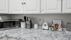 Cucina con mobili bianchi, un forno a microonde, un portachiodi, una macchina da caffè e un libro di cucina sul bancone.