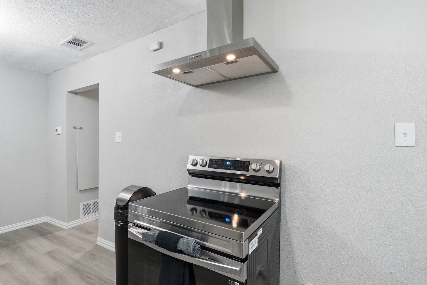 A modern kitchen with a stainless steel oven and a range hood, white walls, and a wooden floor.