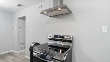 A modern kitchen with a stainless steel oven and a range hood, white walls, and a wooden floor.