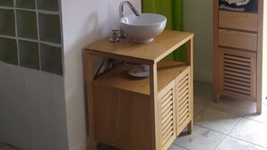 Un baño con lavamanos blanco, espejo, cortina de ducha verde y un mueble de madera con toallas.