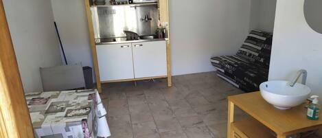 A compact kitchen with a microwave, sink, and storage cabinets. A small dining table with a chair is visible.