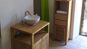 Un baño con tocador de madera, un lavabo blanco, un espejo, cortina de ducha verde y un armario de madera con una caja etiquetada “Livebox 4”.