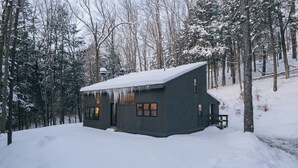 Eine Hütte mit schneebedecktem Dach, umgeben von einem Wald.