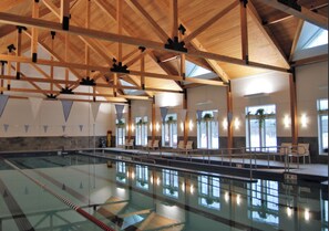 A large indoor swimming pool with clear lanes, wooden beams, and seating areas.