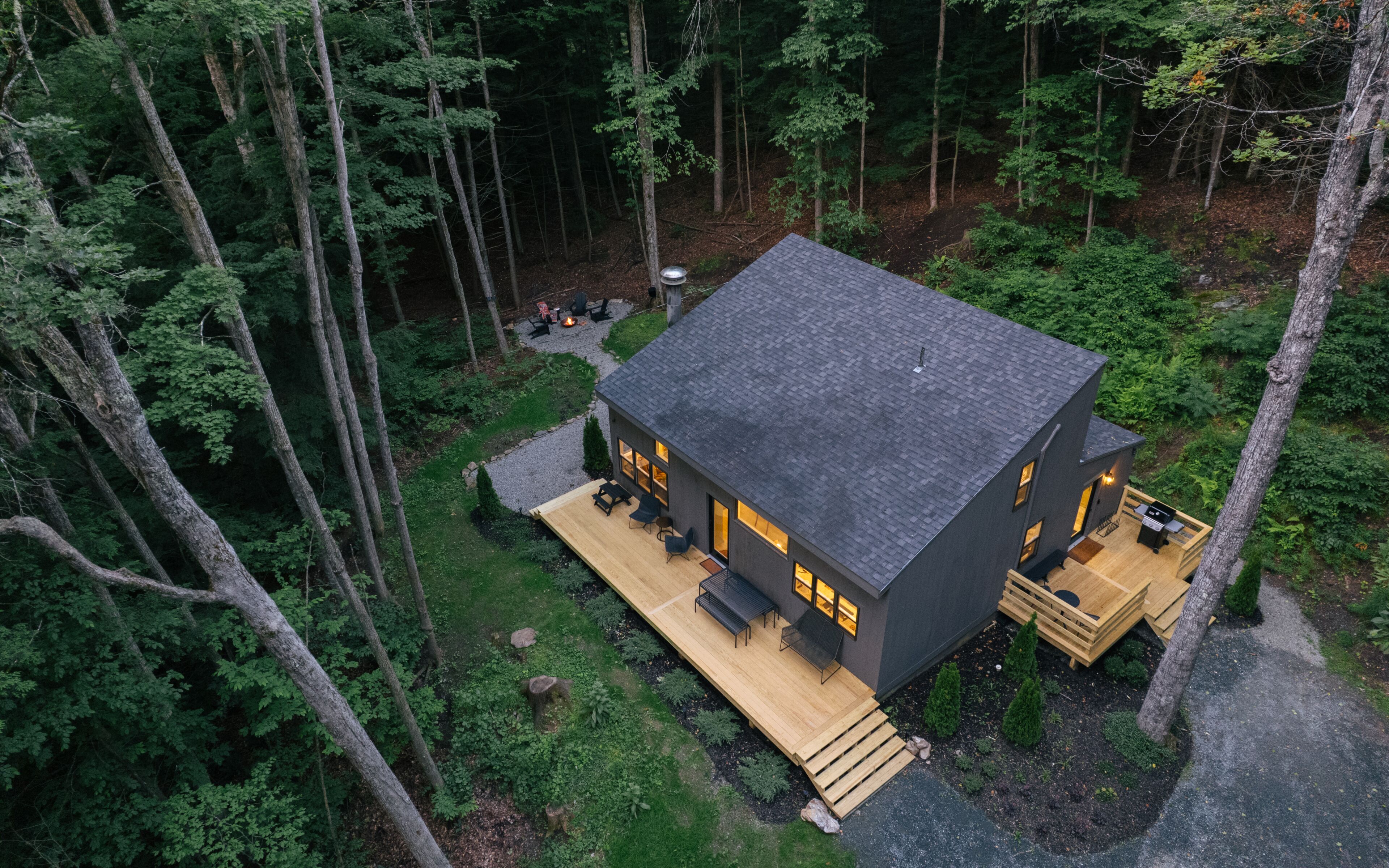 A modern house with a deck, surrounded by a forest.