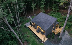 A modern house with a deck, surrounded by a forest.