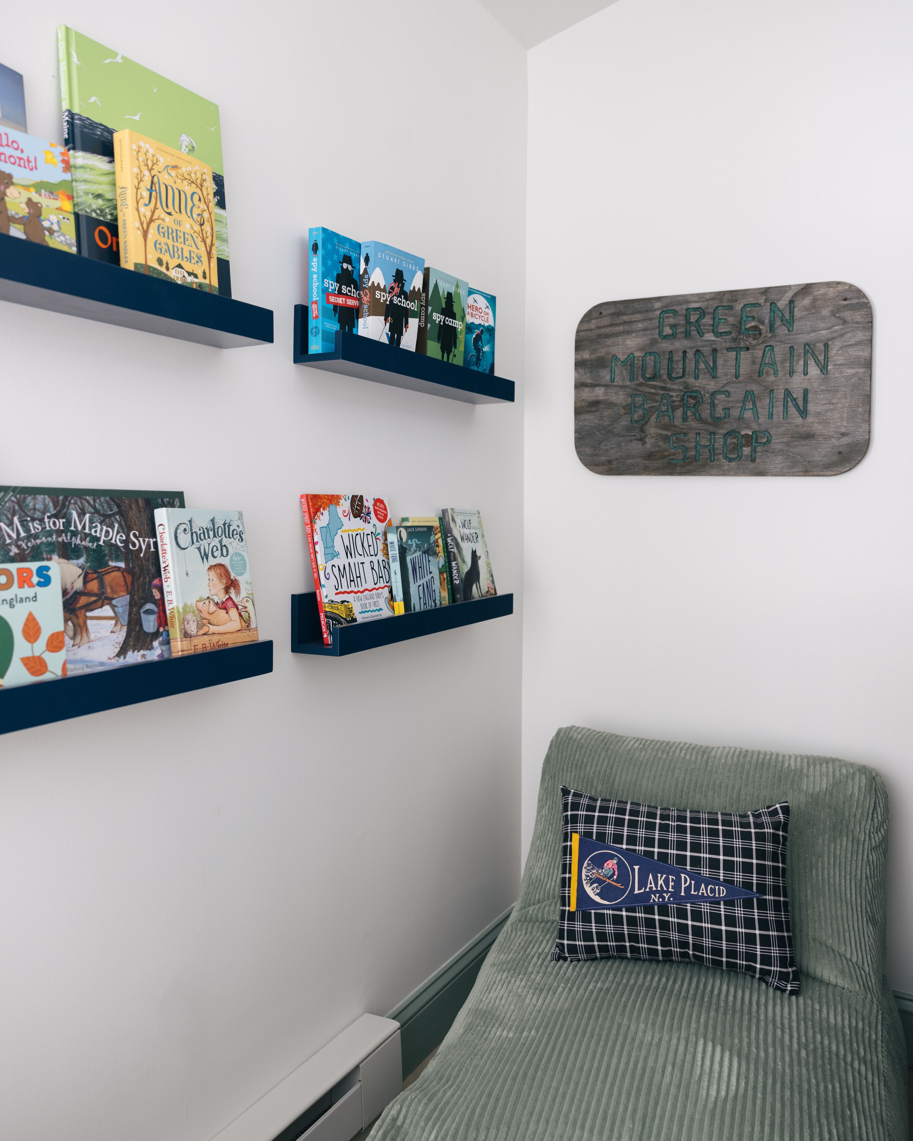 A room with a green couch, a pillow with a logo, and shelves with books and a wooden sign.