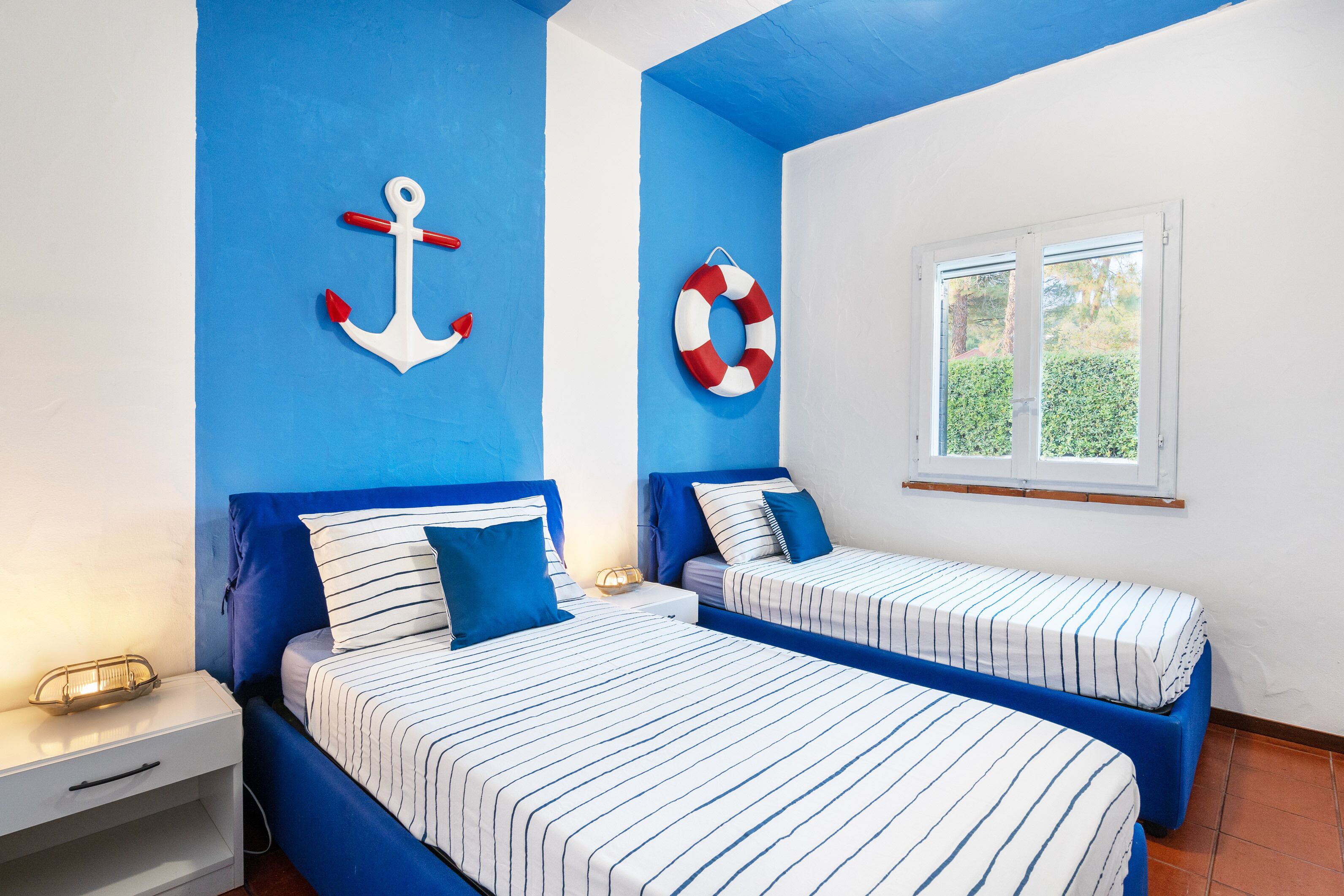A room with two beds, blue walls, a window, and nautical-themed decor.