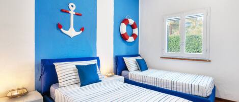 A room with two beds, blue walls, a window, and nautical-themed decor.
