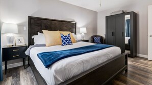 Quarto moderno com uma cama grande, cabeceira em madeira escura, duas mesas de cabeceira com luminárias, um guarda-roupa e um ventilador de teto.