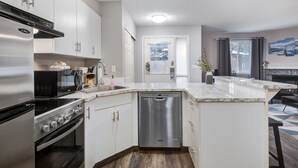 Cozinha moderna com eletrodomésticos de aço inoxidável, armários brancos e bancada de mármore.