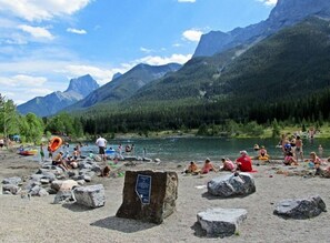 Ein felsiger Strand mit Menschen, die sich an Wassersportaktivitäten beteiligen, umgeben von Bergen und einem klaren Himmel.